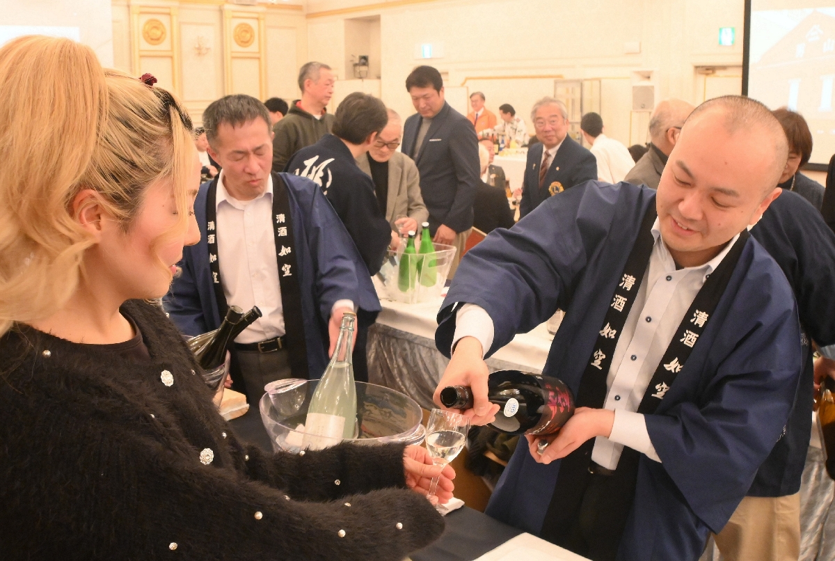 酒造関係者（右）からグラスに地酒をついでもらう参加者