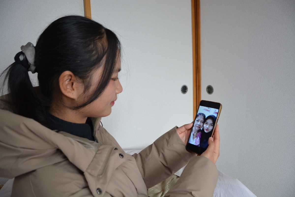 休憩中に母親と撮った写真を見つめるメリナ・ワティさん=3月中旬、八戸市