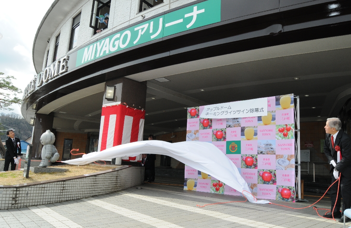 新名称を覆っていた白い布を除幕する泉山元社長(右)