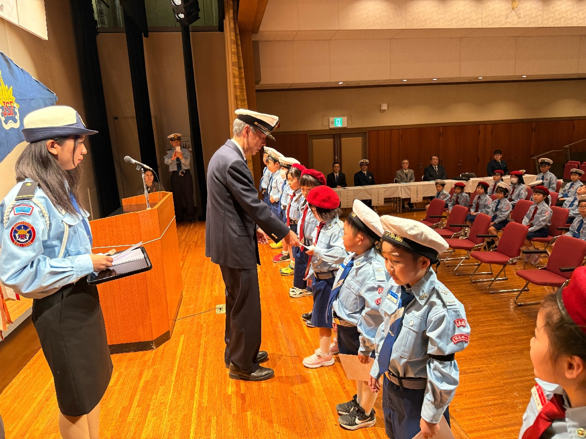 浮木隆団長（中央）から団員証を受け取る児童（八戸市海洋少年団提供）