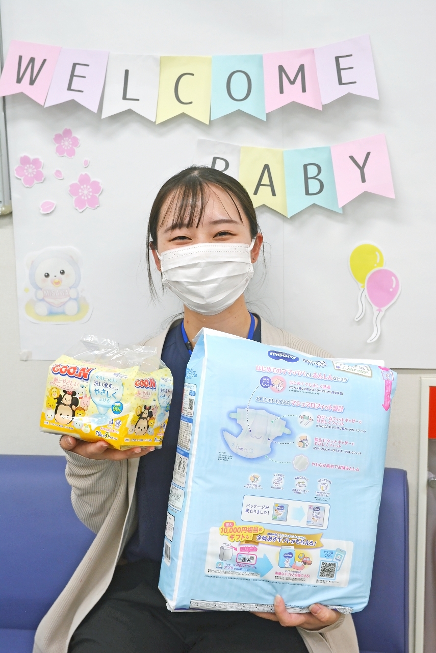 記念撮影用のコーナーで、配布する子育て用品を手にする職員