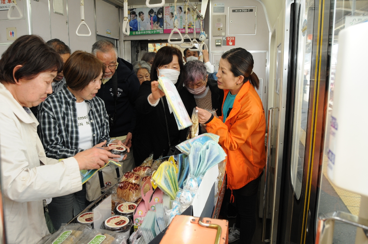 ラッピングトレイン内で三戸町の土産物を買い求めるツアー参加者