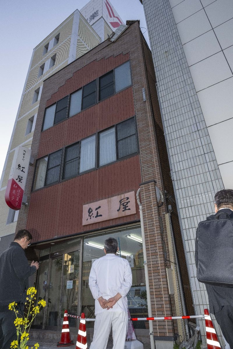 隣のビルから崩れた壁面パネルを不安そうに見上げる関係者=20日午後5時半すぎ、八戸市廿三日町