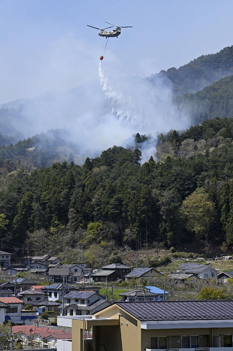 岩手県大槌町の山林火災で、民家近くの山で消火活動に当たるヘリコプター=25日午前