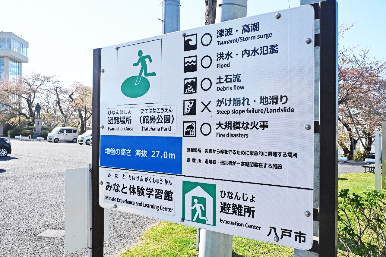 館鼻公園に設置されている看板。公園は「避難場所」、敷地内にあるみなと体験学習館は「避難所」とだけ示されている=25日、八戸市