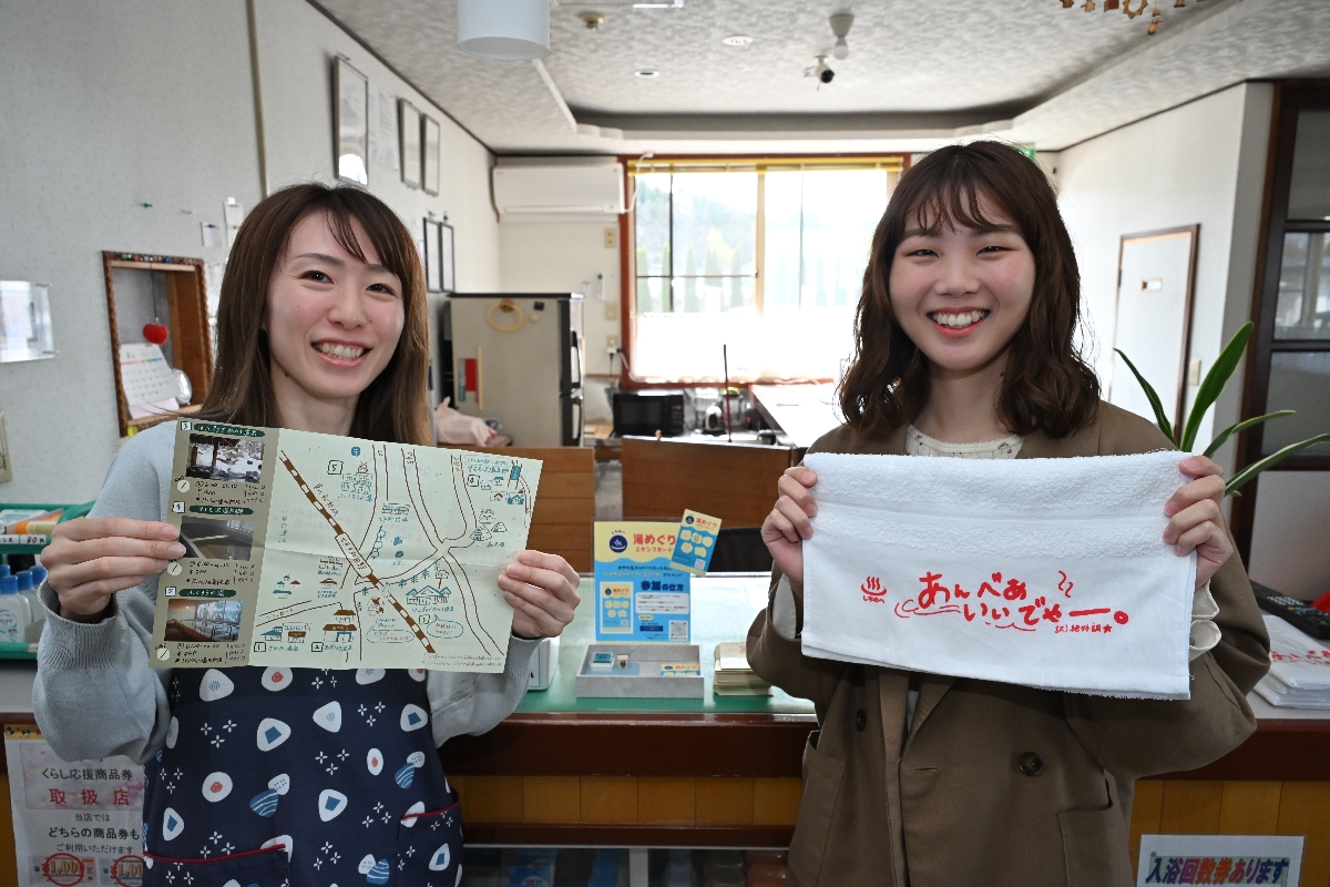 七戸町内温泉施設のマップを制作し、スタンプラリーも企画した地域おこし協力隊の吉澤莉沙さん（右）。手に持つのは五つの施設を回るともらえる吉澤さんデザインのタオル
