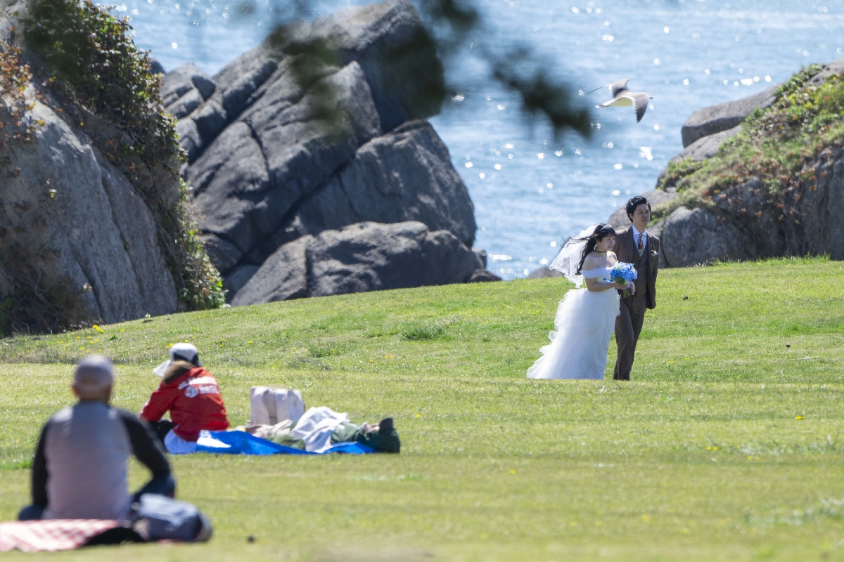 種差の美しい海をバックに結婚式の前撮りをするカップル（右上）＝５日、八戸市