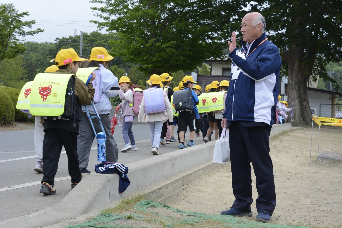 クマ対策グッズを手に下校する子どもたちを見守る皆川智希校長=21日、八戸市立町畑小