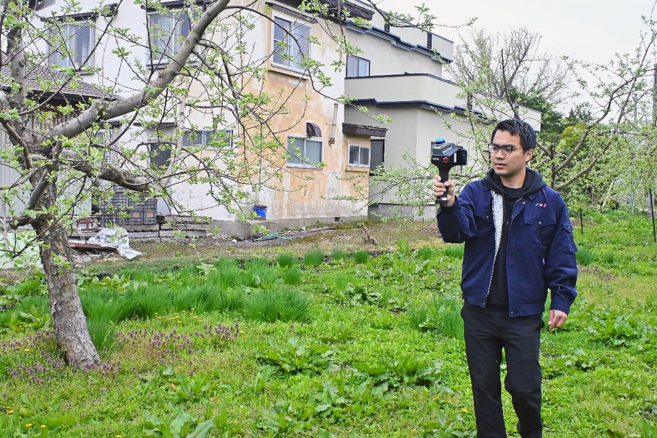 リンゴ園地を3Dスキャナーで撮影する佐々木佑介代表=4月28日、弘前市
