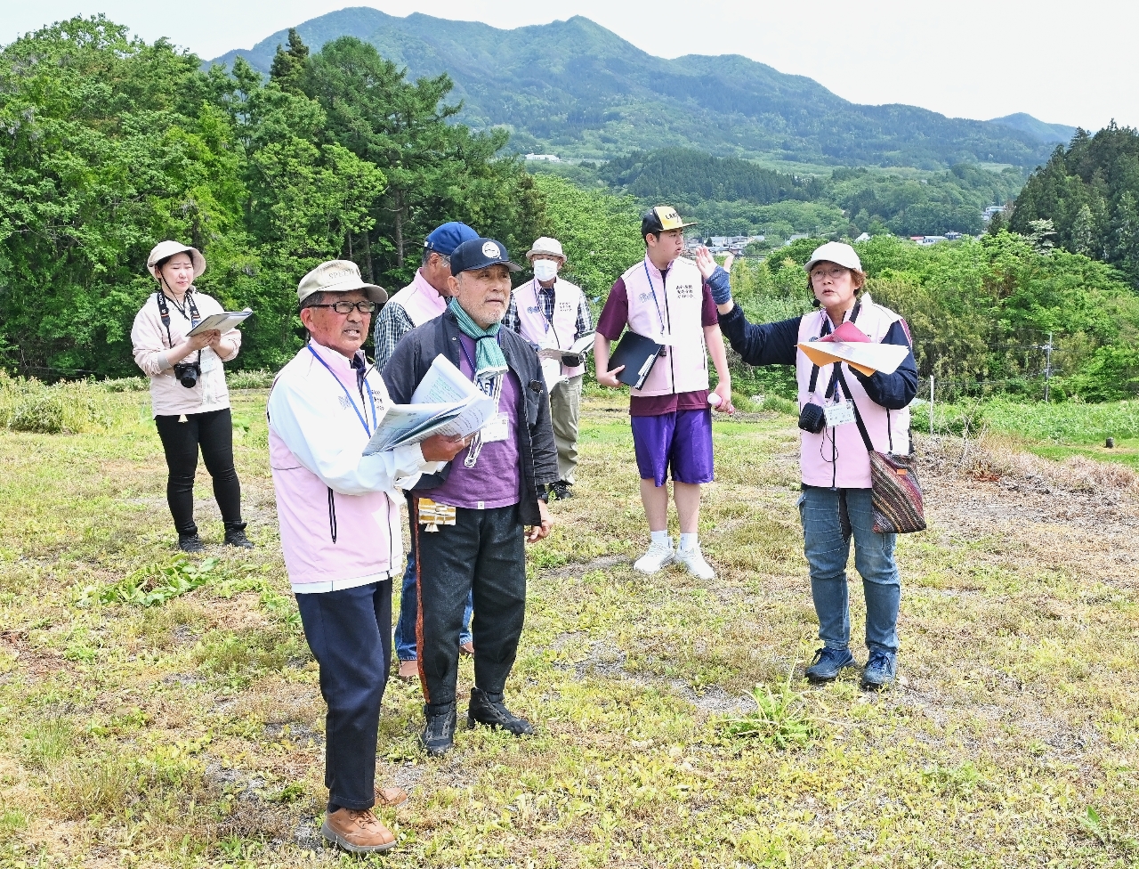 ガイドブックを参考に発掘現場を案内する松本佳江さん(右)