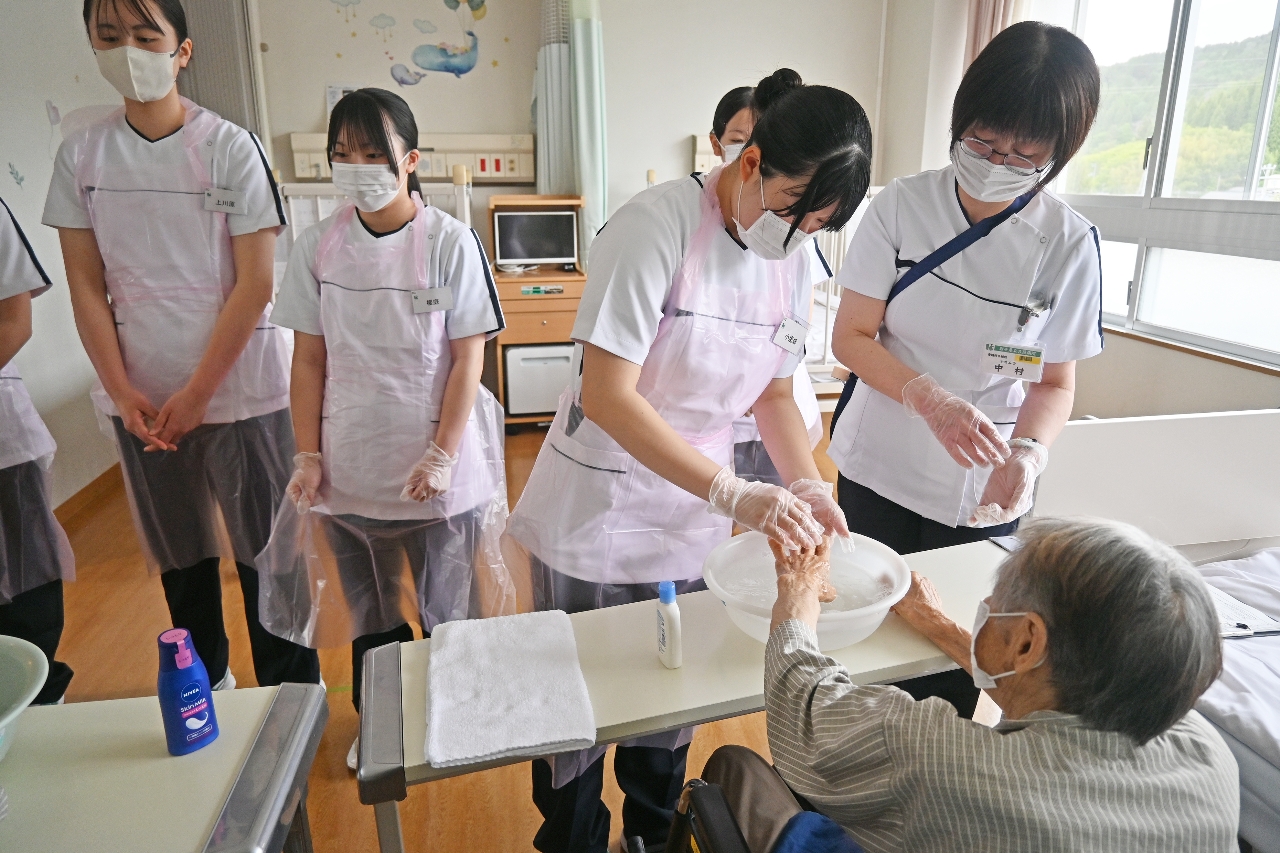 看護師のアドバイスを聞きながら、入院患者の手を洗う高校生