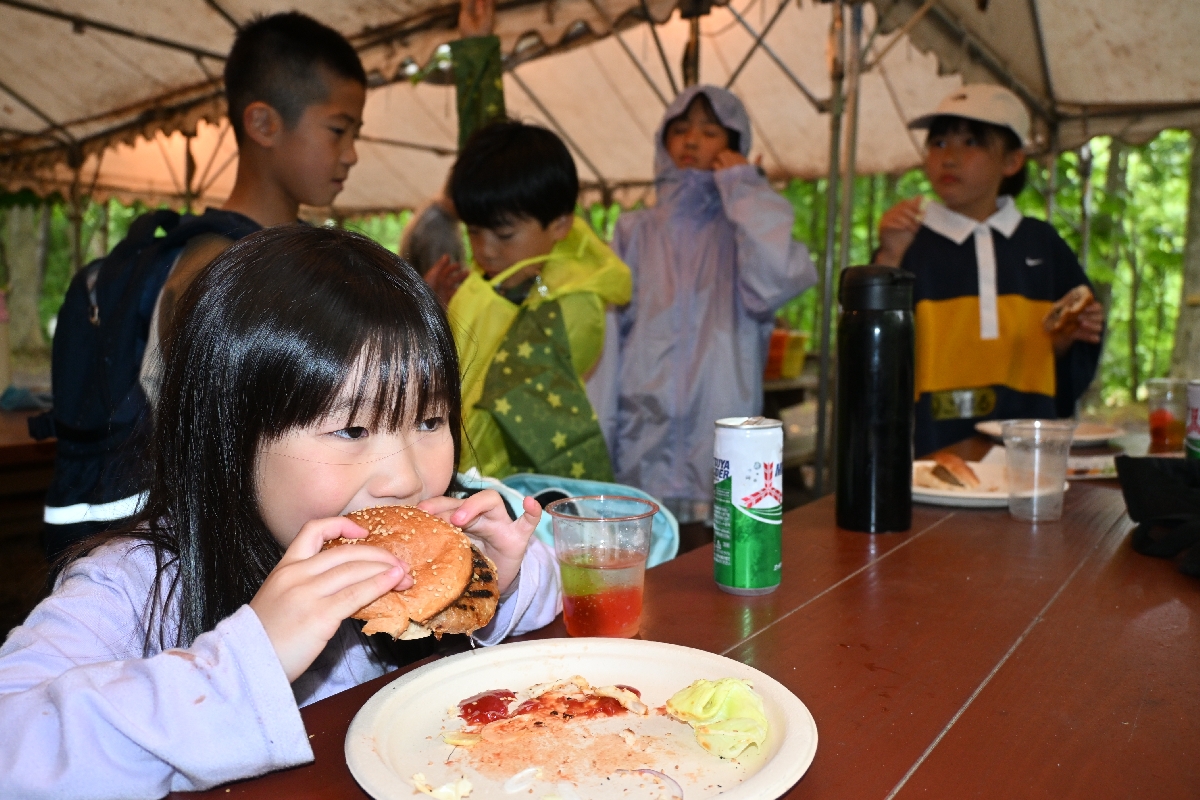 昼食に作ったハンバーガーを頰張る児童