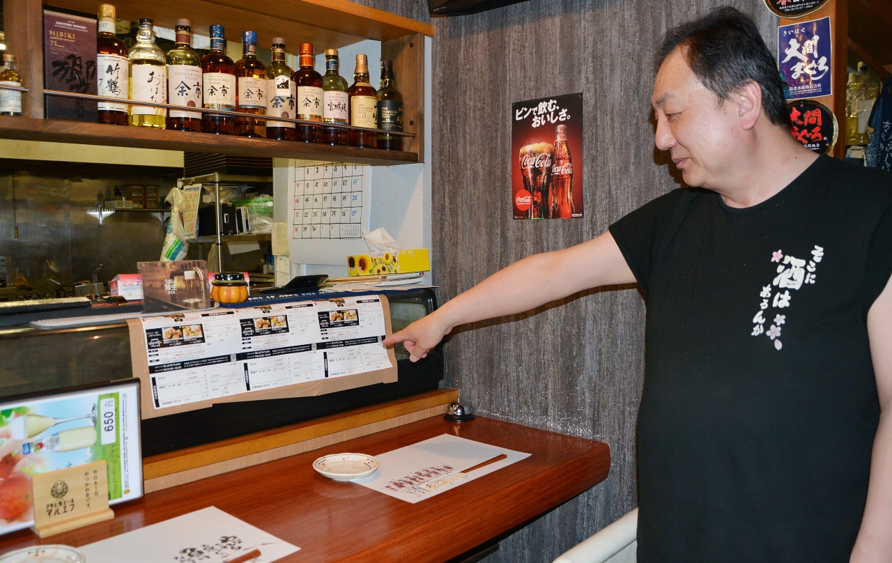 地震でガラスが割れたままのネタケースを指し示す竹中亨考さん=2日、八戸市十三日町