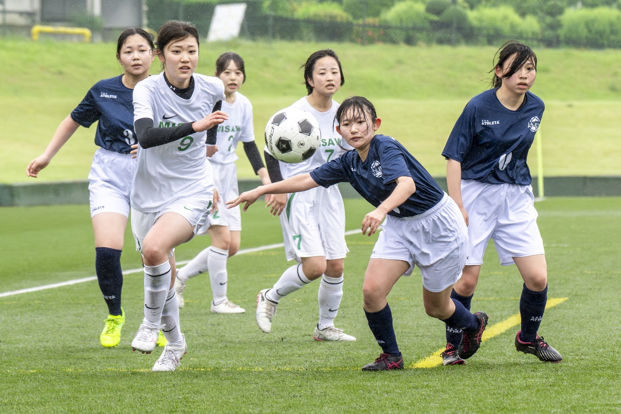 サッカー女子１回戦で、勝利を目指して熱戦を繰り広げる三沢、三本木の選手たち＝５日、五戸町ひばり野運動公園サッカー場