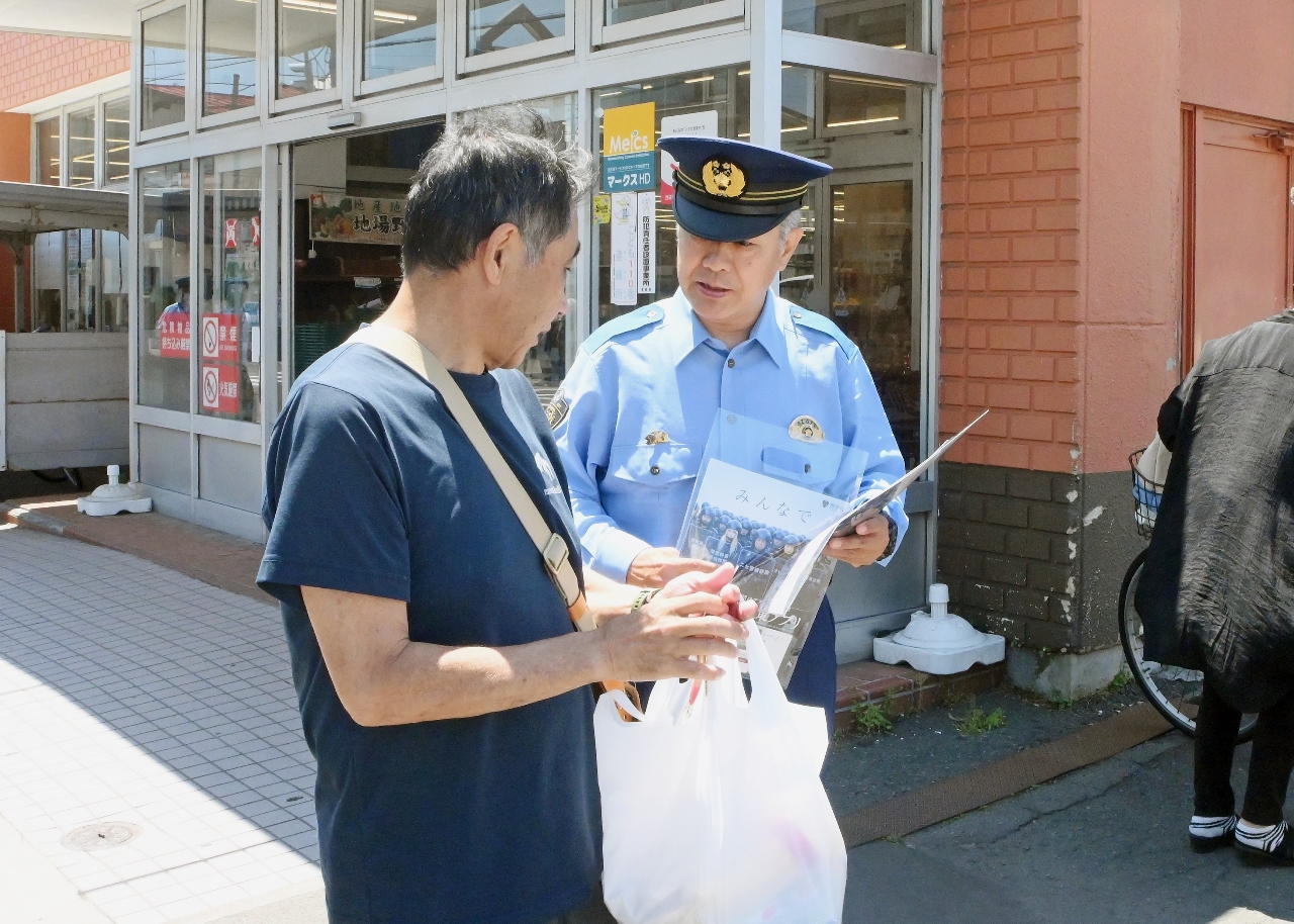 スーパーの来店客(左)に情報提供を呼びかける警察幹部=17日、青森市