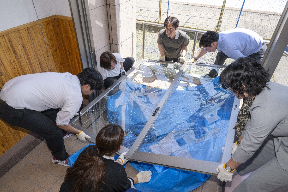 倒壊したガラス製の戸を片付ける職員=25日、八戸市立旭ヶ丘小学校