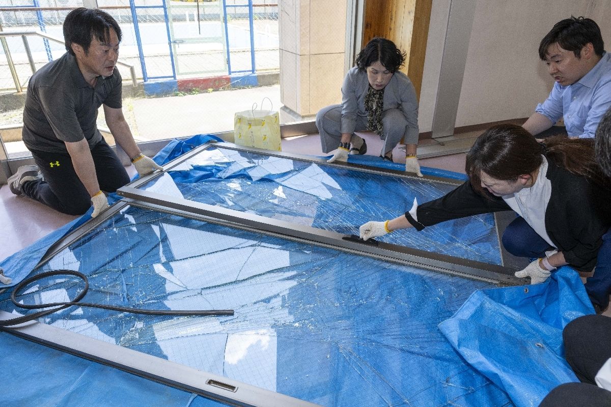倒壊したガラス製のドアを片付ける職員＝２５日、八戸市立旭ヶ丘小学校