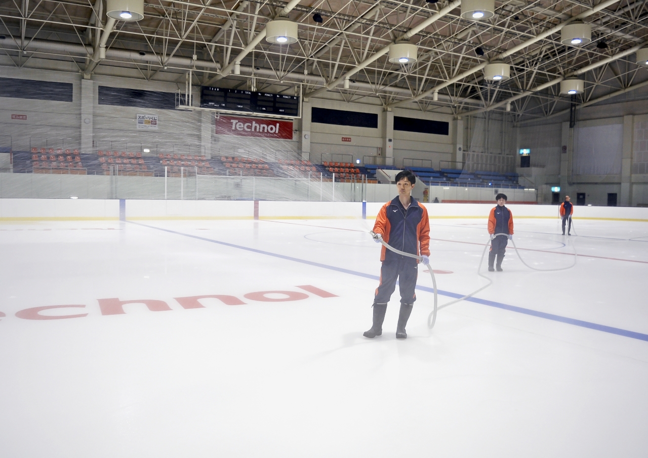 リンクにお湯をまいて氷作りに励むスタッフ=8日、テクノルアイスパーク八戸