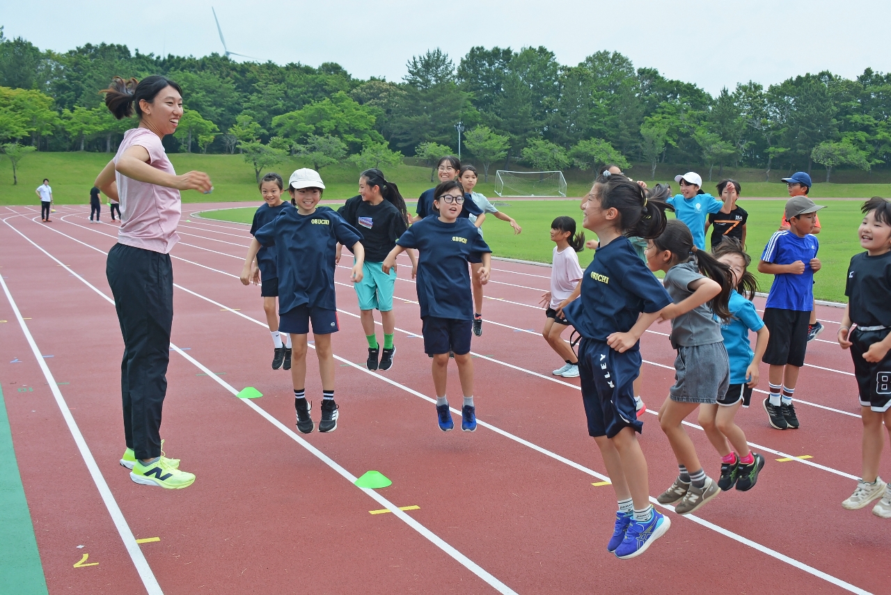 益子芽里選手(左)と一緒に飛びはねる児童