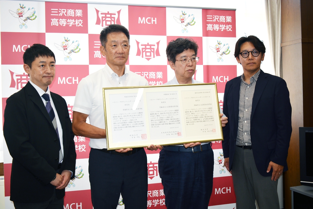 指定証を手にする小島一富士代表理事（中央右）と豊川武伸校長（同左）＝１６日、三沢商業高