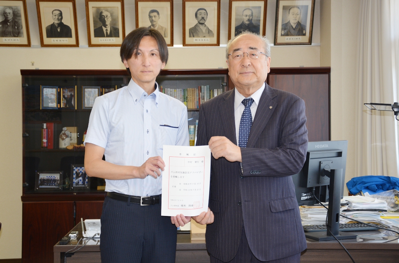 気象防災アドバイザーの委嘱状を手にする中村智行さん（左）と橋本隆春村長＝１６日、六ケ所村