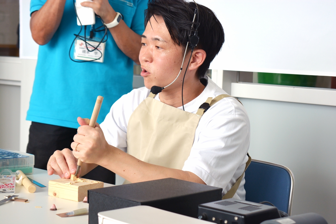 来場者とトークしながら木彫りを実演するキボリノコンノさん