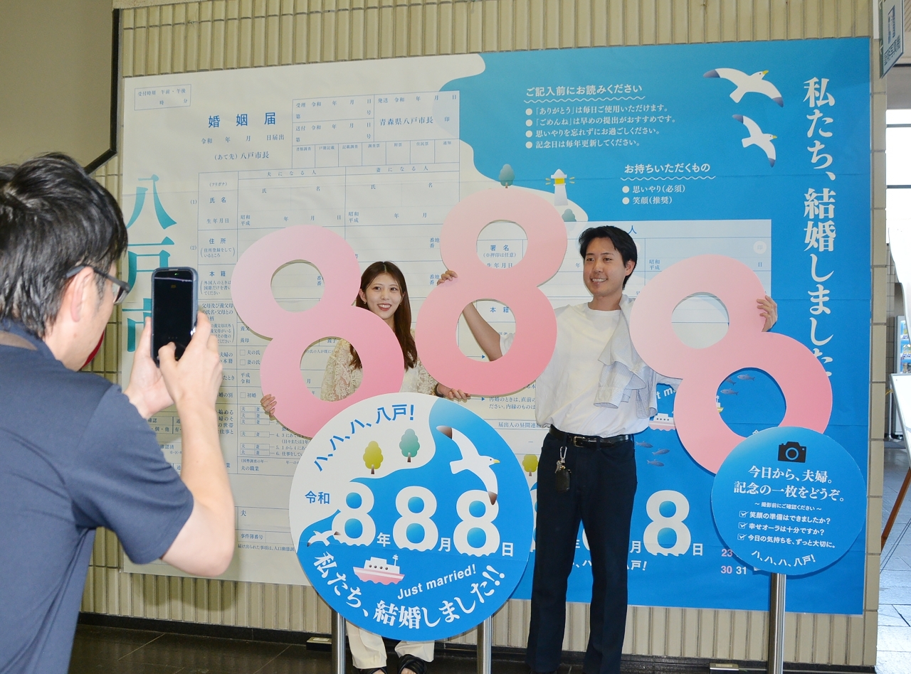 婚姻届を提出し特設パネルの前で記念撮影するカップル＝８日、八戸市庁