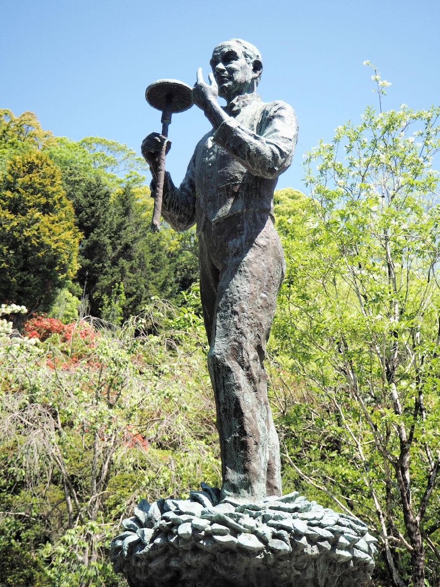 大きなキノコを持つ牧野富太郎の銅像。足元には草も=高知市の高知県立牧野植物園