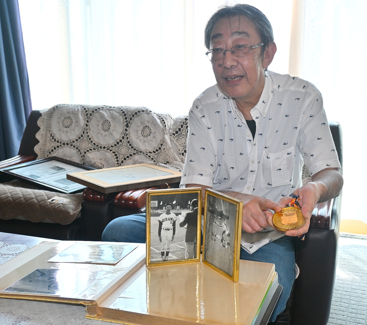 軟式野球少年で優勝した青森(三沢木崎野メッツ)の主将を務めた久保田昭さん。当時の写真や金メダルを見返しながら思い出を語る=6日、東北町