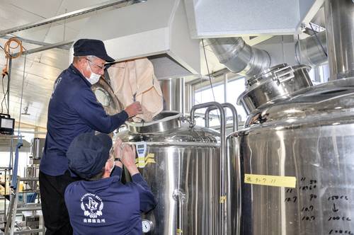 粉砕した麦芽を釜に投入する山形琢一社長(左)=23日、八戸市南郷