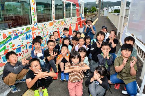 自分たちのイラストで彩られた車両の前で喜ぶ児童たちと井上信太さん(奥)
