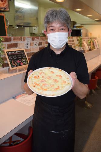 看板メニューとなっている独自製法のピザをアピールする山一義信さん