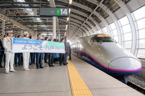東北新幹線八戸開業20周年を記念した特別運行で、八戸駅に到着したE2系車両「はやて」。関係者が横断幕を手に出迎えた=3日午前11時22分