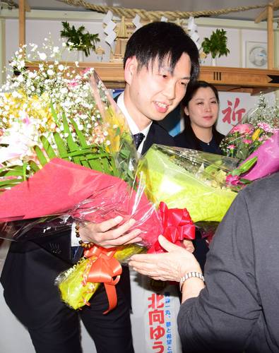 初当選を祝う花束を受け取り、笑顔を見せる北向由樹さん(左)=9日午後10時半ごろ、おいらせ町内の事務所