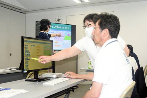 総会でプログラミング教材「スクラッチ」の操作を体験する松尾和彦会長(右)