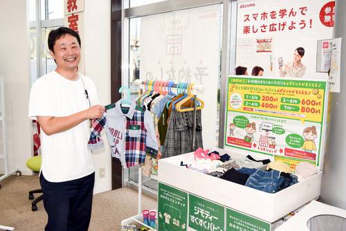 ドコモショップ八戸下長店に設置した「ジモティーすくすくバトン」のコーナーをPRする遠藤慎治店長=19日、八戸市