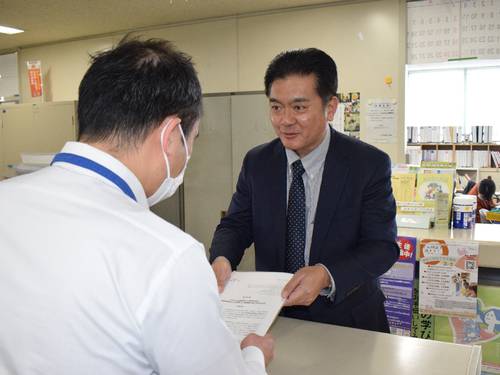 八戸市広報統計課の担当者(手前)に要望書を手渡す小倉謙支部長=12日、市庁