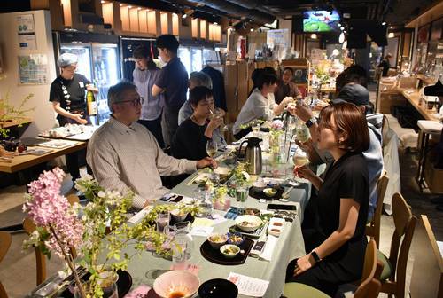 長いテーブルを囲み、八戸地域の食材と酒を楽しむ鷹野麗さん(手前右)と参加者=4月下旬、東京