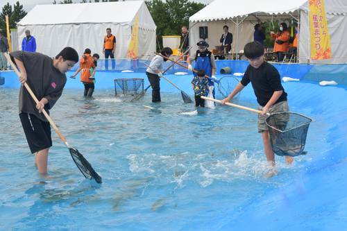 網を持っていけすに入り、魚を追う子どもたち=18日、六ケ所村