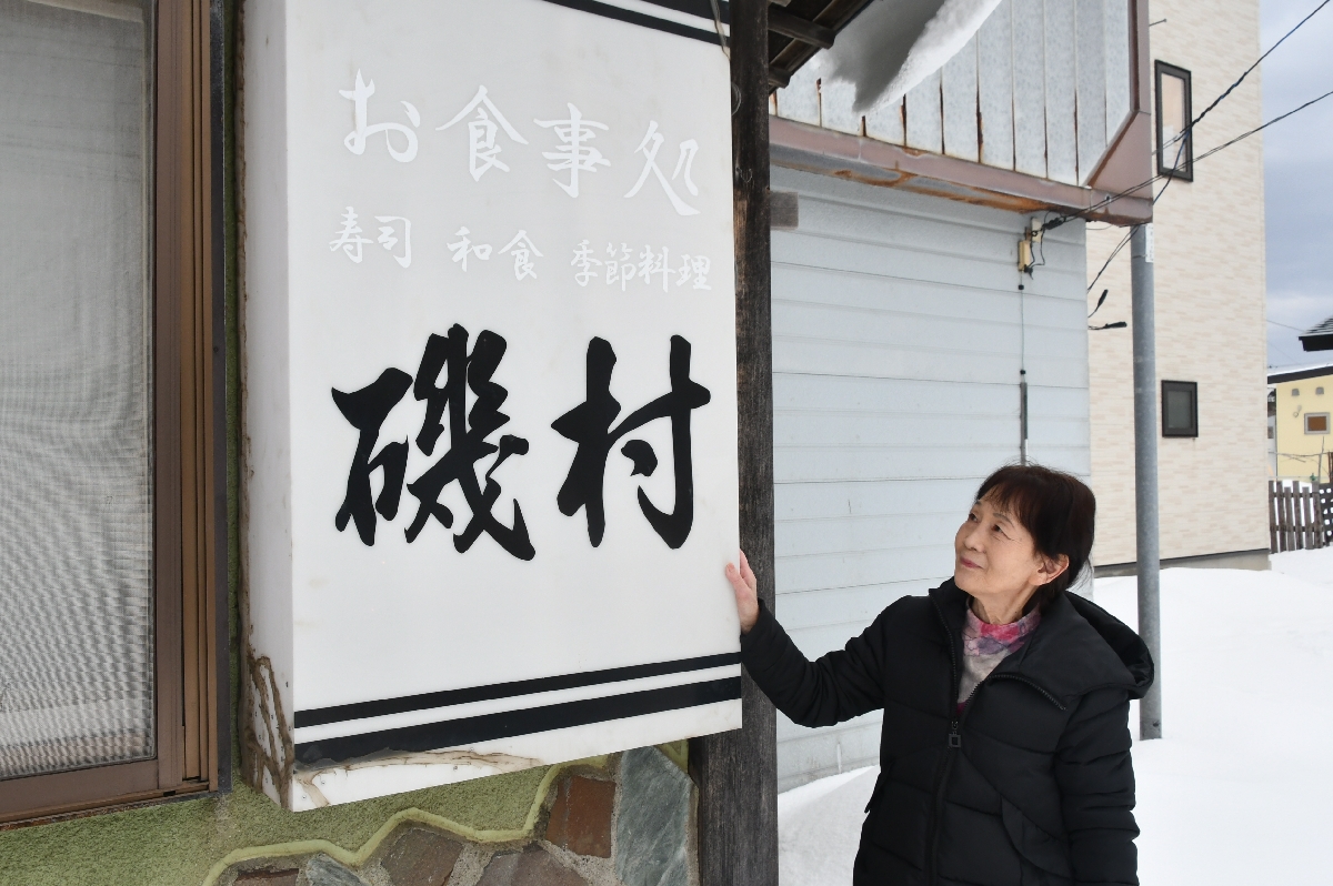 閉店した店の看板を見つめる沼辺しげ子さん=2月、六ケ所村