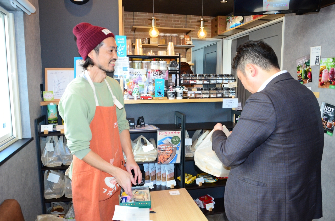顔なじみの客にテイクアウトの料理を渡す堀井隆之さん(左)。何気ない会話に笑みがこぼれた=17日午後0時5分ごろ、八戸市小中野2丁目のカフェ「LEAVES」